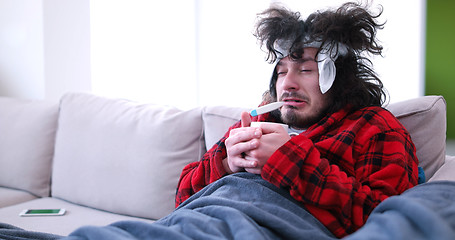 Image showing sick man is holding a cup while sitting on couch
