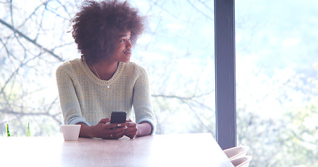 Image showing black woman drinking coffee and using a mobile phone  at home