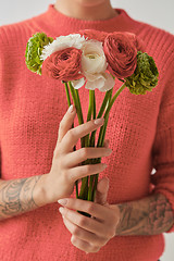 Image showing Young girl in a sweater in a color of the year 2019 Living Coral Pantone holding a bouquet of fresh flowers in her hands with tatoo.