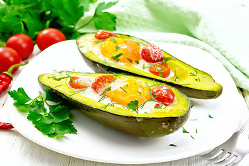 Image showing Scrambled eggs with tomatoes in avocado on light wooden board