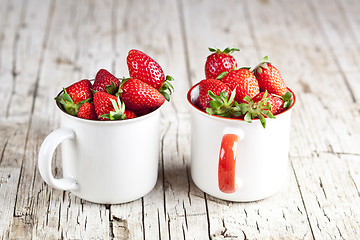 Image showing Organic red strawberries in two white ceramic cups on rustic woo