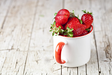 Image showing Organic red strawberries in white ceramic cup on rustic wooden b