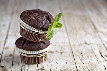 Image showing Chocolate dark muffins with mint leaves on rustic wooden table.