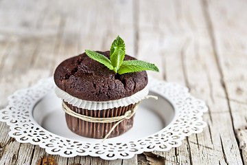 Image showing Fresh dark chocolate muffin with mint leaves on white plate on r