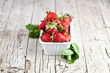 Image showing Fresh red strawberries in white bowl and mint leaves on rustic w