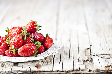 Image showing Red strawberries on white plate on rustic wooden background.