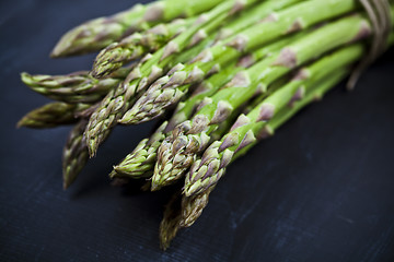 Image showing Bunch of fresh raw garden asparagus closeup on black board backg