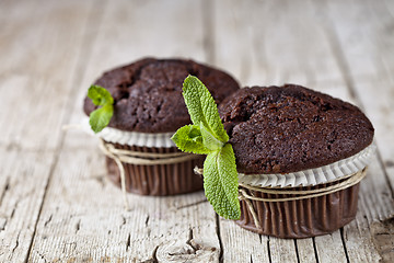 Image showing Chocolate dark muffins with mint leaves closeup on rustic wooden