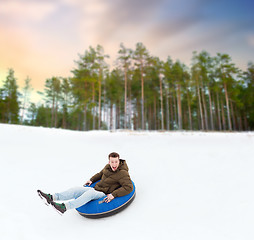 Image showing happy young man sliding down hill on snow tube