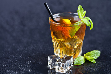 Image showing Iced tea with lemon, mint leaves and ice cubes in glass on wet b