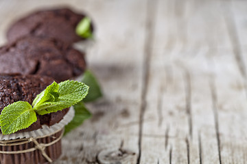 Image showing Chocolate dark muffins with mint leaves closeup on rustic wooden