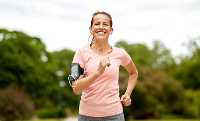 Image showing woman with earphones add armband jogging at park