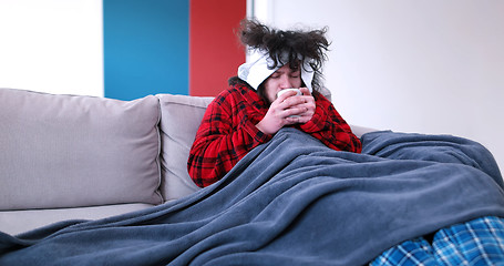 Image showing sick man is holding a cup while sitting on couch