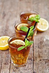 Image showing Cold iced tea with lemon, mint leaves and ice cubes in three gla
