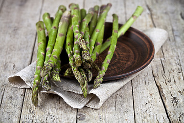 Image showing Fresh raw garden asparagus closeup on brown ceramic plate and li