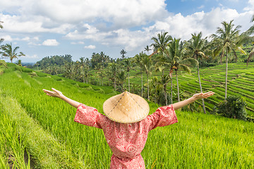 Image showing Relaxed fashionable caucasian woman wearing red asian style kimono and traditional asian paddy hat, arms rised to sky, enjoying pure nature at beautiful green rice fields on Bali island