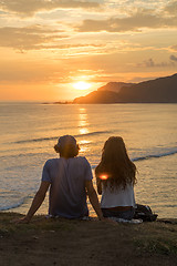 Image showing Romantic couple on vacation sitting and watching colorful sunset over the sea coast.