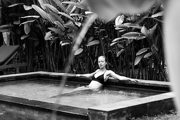 Image showing Sensual young woman relaxing in outdoor spa infinity swimming pool surrounded with lush tropical greenery of Ubud, Bali. Black and white image.