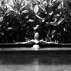 Image showing Sensual young woman relaxing in outdoor spa infinity swimming pool surrounded with lush tropical greenery of Ubud, Bali. Black and white image.