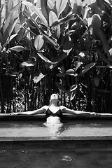 Image showing Sensual young woman relaxing in outdoor spa infinity swimming pool surrounded with lush tropical greenery of Ubud, Bali. Black and white image.