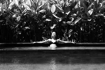 Image showing Sensual young woman relaxing in outdoor spa infinity swimming pool surrounded with lush tropical greenery of Ubud, Bali. Black and white image.