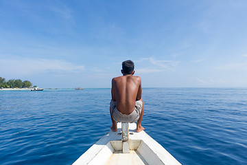 Image showing Local Sporty Guy Sitting Topless at the Bow of Traditional White Wooden Sail Boat, Looking At Beautiful Blue Sea of Gili Islands near Bali, Indonesia