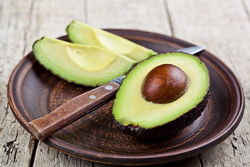 Image showing Fresh organic avocado on ceramic plate and knife on rustic woode