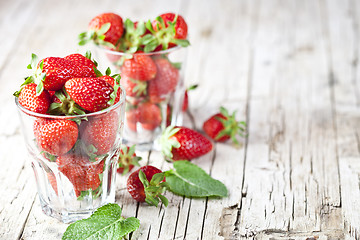 Image showing Organic red strawberries in glass and mint leaves on rustic wood