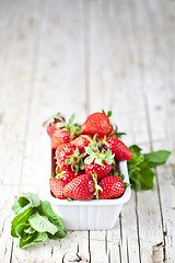 Image showing Fresh red strawberries in white bowl and mint leaves on rustic w