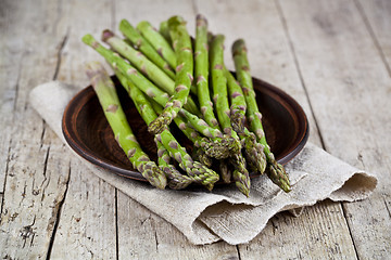 Image showing Fresh raw garden asparagus closeup on brown ceramic plate and li