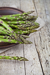 Image showing Fresh raw garden asparagus closeup on brown ceramic plate and li