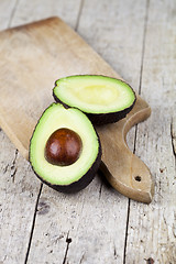 Image showing Fresh organic avocado halves on cutting board on old wooden tabl
