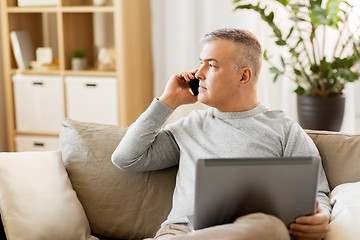 Image showing man with laptop calling on smartphone at home