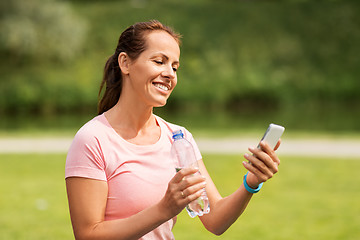 Image showing woman with smartphone drinking water in park