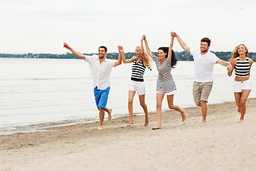 Image showing friends in striped clothes running along beach