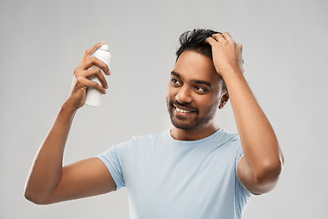 Image showing smiling indian man applying hair spray over gray