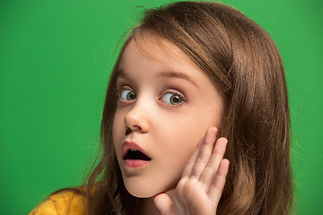 Image showing The young teen girl whispering a secret behind her hand over green background