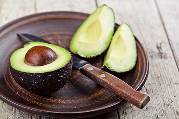 Image showing Fresh organic avocado on ceramic plate and knife on rustic woode