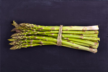 Image showing Bunch of fresh raw garden asparagus on black board background. G