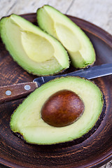 Image showing Fresh organic avocado on ceramic plate and knife on rustic woode