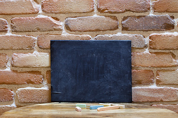 Image showing Blank blackboard on wooden table at brick wall.