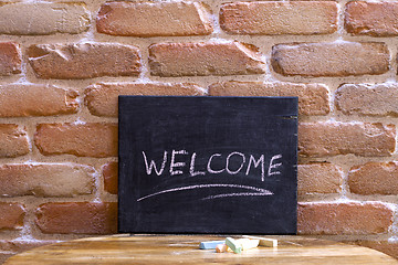 Image showing Black board with the word WELCOME drown by hand on wooden table 