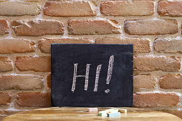 Image showing Black board with the word HI! drown by hand on wooden table on b