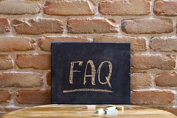 Image showing Black board with the word FAQ drown by hand on wooden table on b