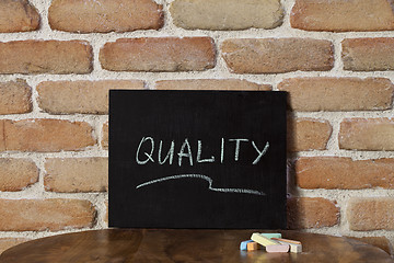 Image showing Chalk board with the word QUALITY drown by hand on wooden table 