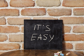 Image showing Black board with the phrase IT'S EASY drown by hand on wooden ta