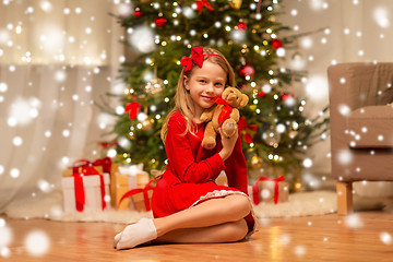 Image showing girl in red dress hugging teddy bear at home