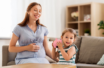 Image showing pregnant mother and daughter with piggy bank