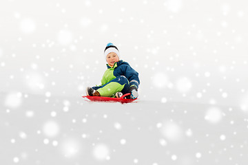 Image showing happy boy sliding on sled down snow hill in winter