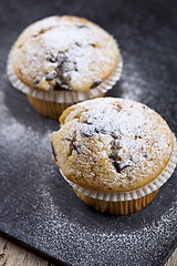 Image showing Two fresh homemade muffins with sugar powder closeup on black bo